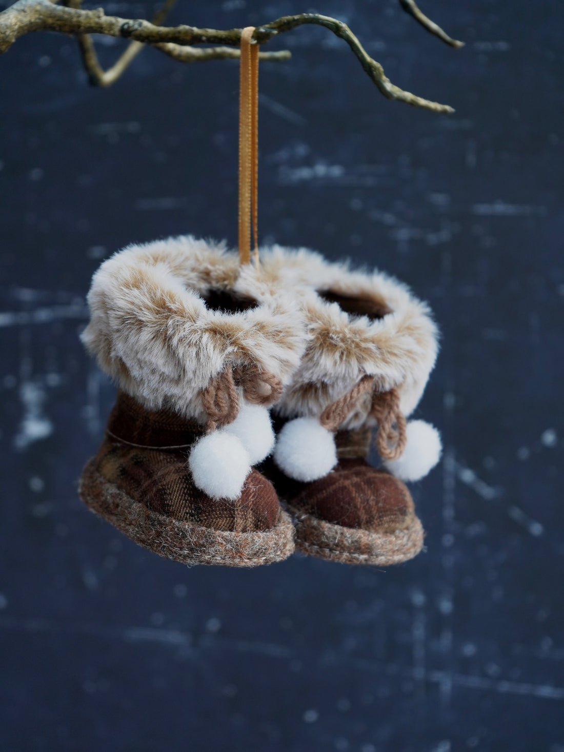 Pair of brown slippers with fur trim hanging from a branch against a snowy background