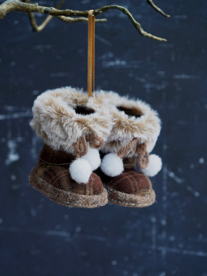 Pair of brown slippers with fur trim hanging from a branch against a snowy background