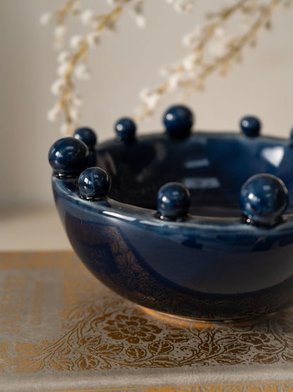 Blue ceramic bowl with spherical bobble protrusions on a decorative surface