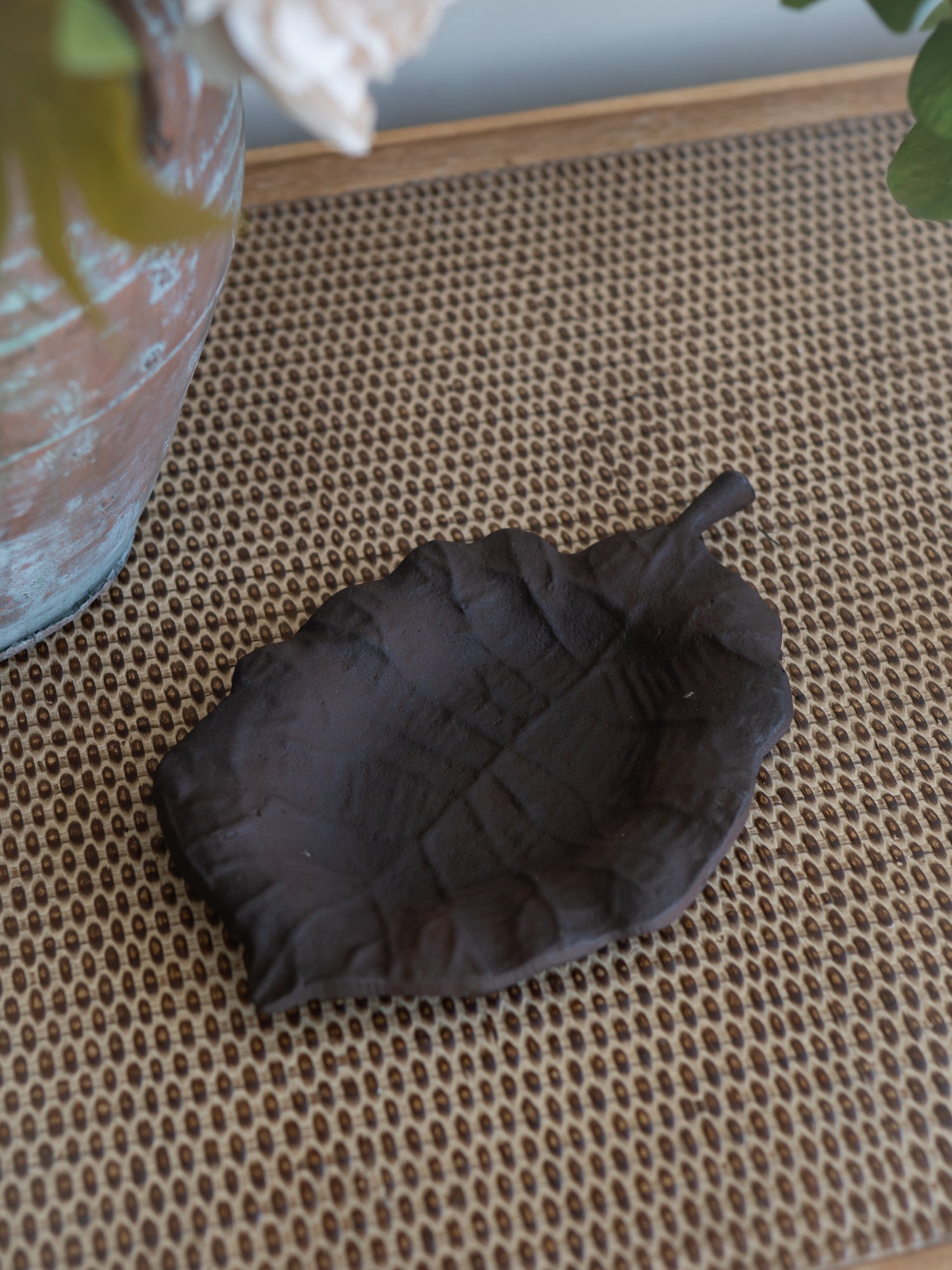 A dark brown leaf-shaped dish or tray with a textured, embossed leaf pattern, resting on a woven brown mat.