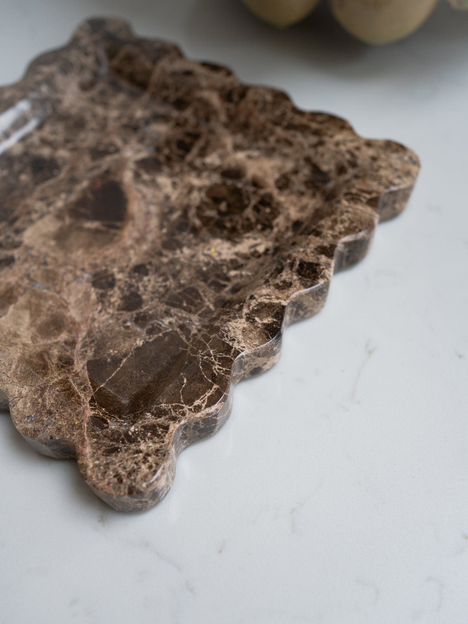 Decorative brown scalloped marble tray with a leaf pattern on a light gray surface