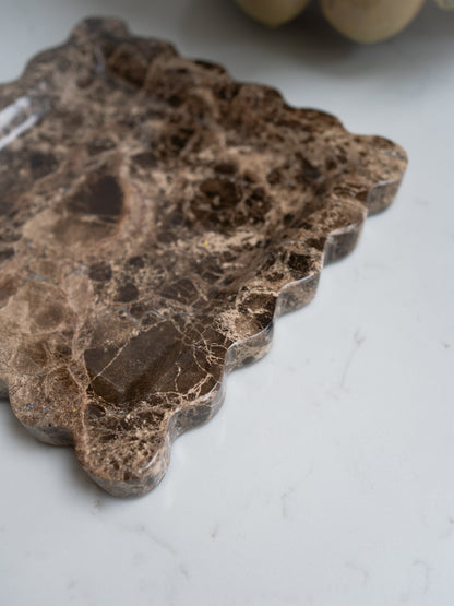 Decorative brown scalloped marble tray with a leaf pattern on a light gray surface