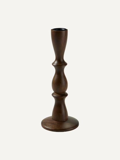 A dark brown wooden candlestick with a turned, sculptural design and a round base, shown against a plain off-white background.