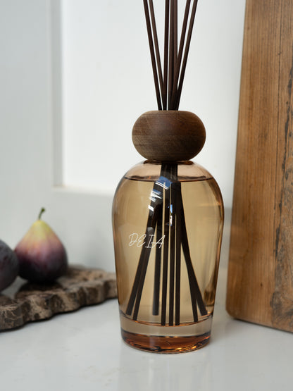 A diffuser bottle with wooden cap and reeds on a white surface.