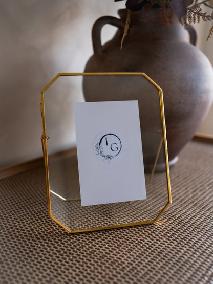 Gold geometric photo frame with a white card featuring a logo on a textured surface.