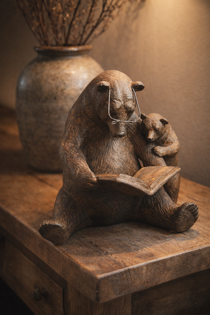 Statue of a bear reading a book to a cub on a wooden surface.