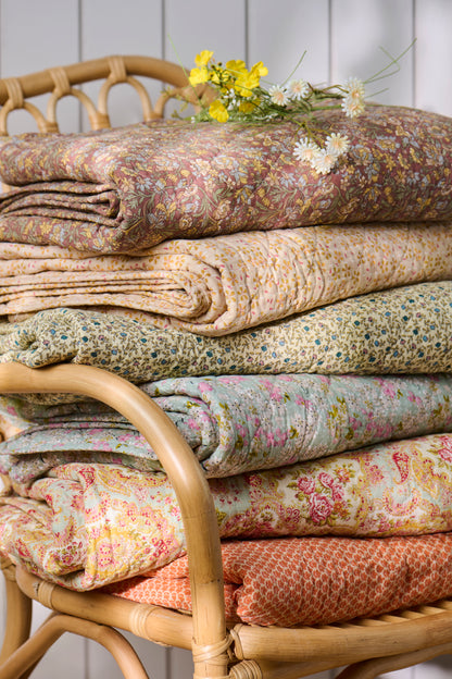 Stack of floral-patterned fabrics on a wicker chair with a white wooden panel background