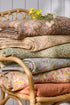 Stack of floral-patterned fabrics on a wicker chair with a white wooden panel background