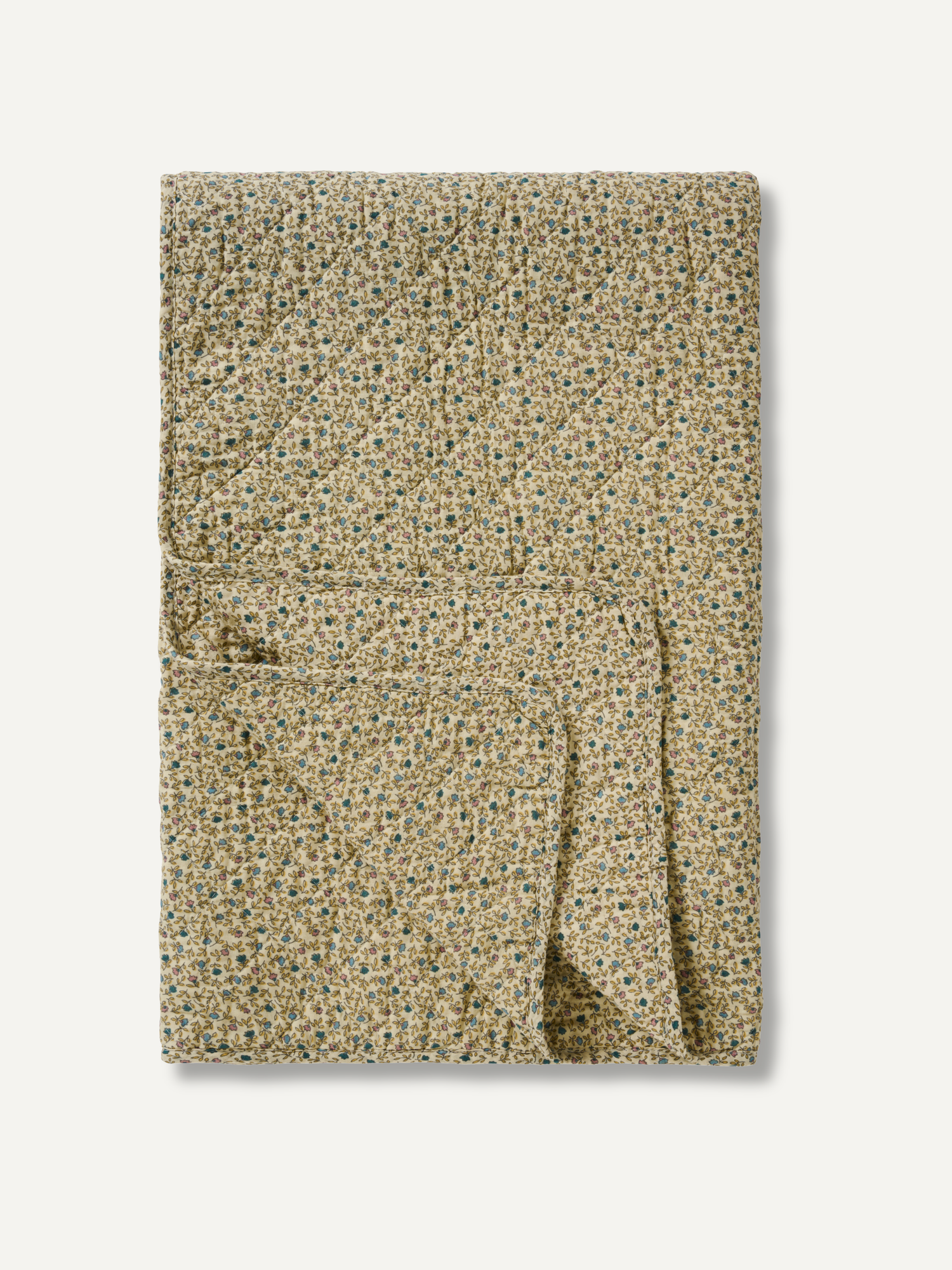 A folded quilted blanket with a dense, small-scale floral pattern in beige, green, and blue, set against a plain off-white background.