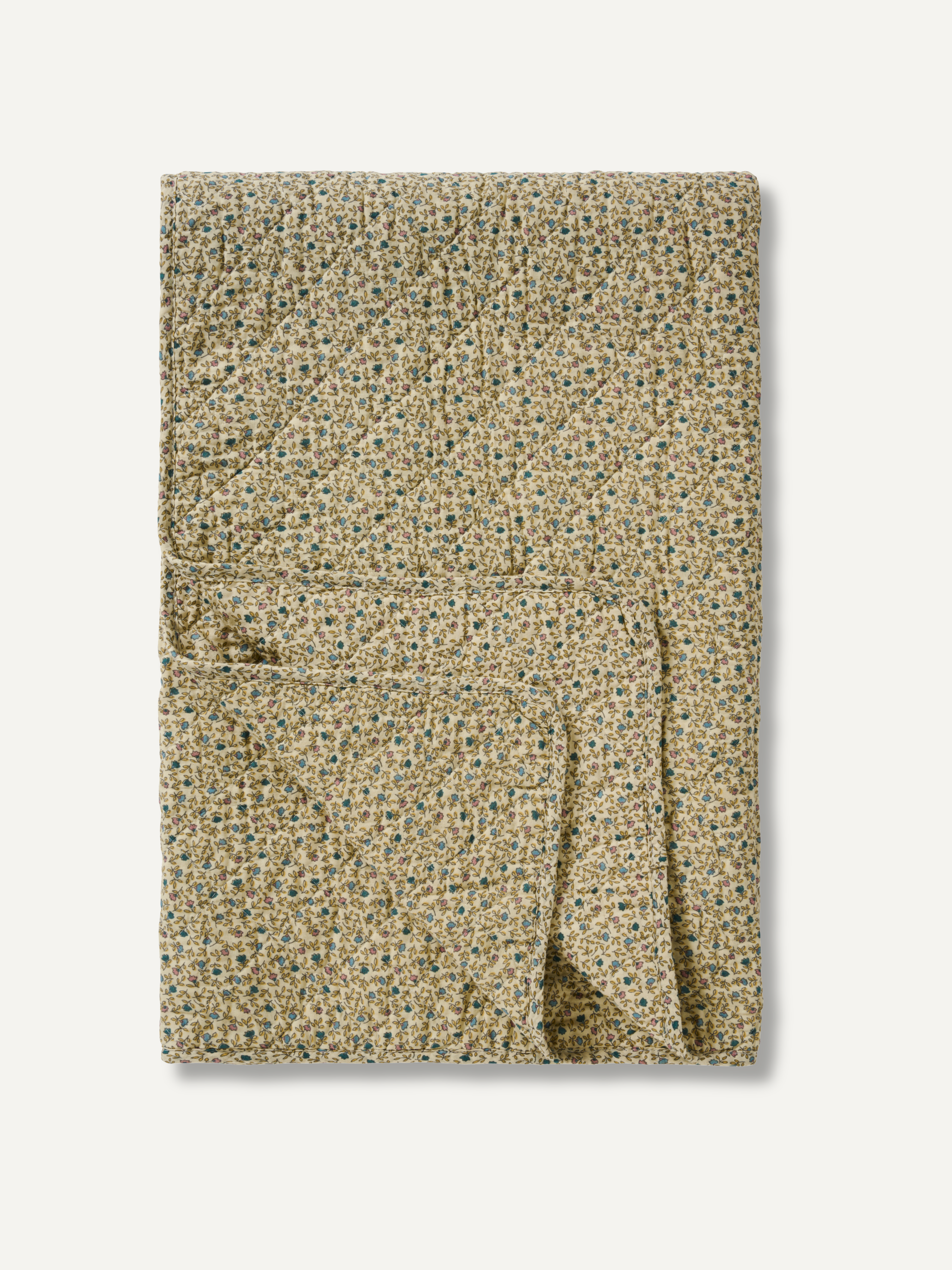 A folded quilted blanket with a dense, small-scale floral pattern in beige, green, and blue, set against a plain off-white background.