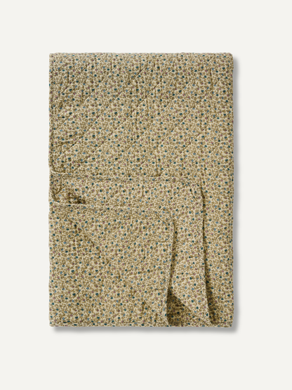A folded quilted blanket with a dense, small-scale floral pattern in beige, green, and blue, set against a plain off-white background.