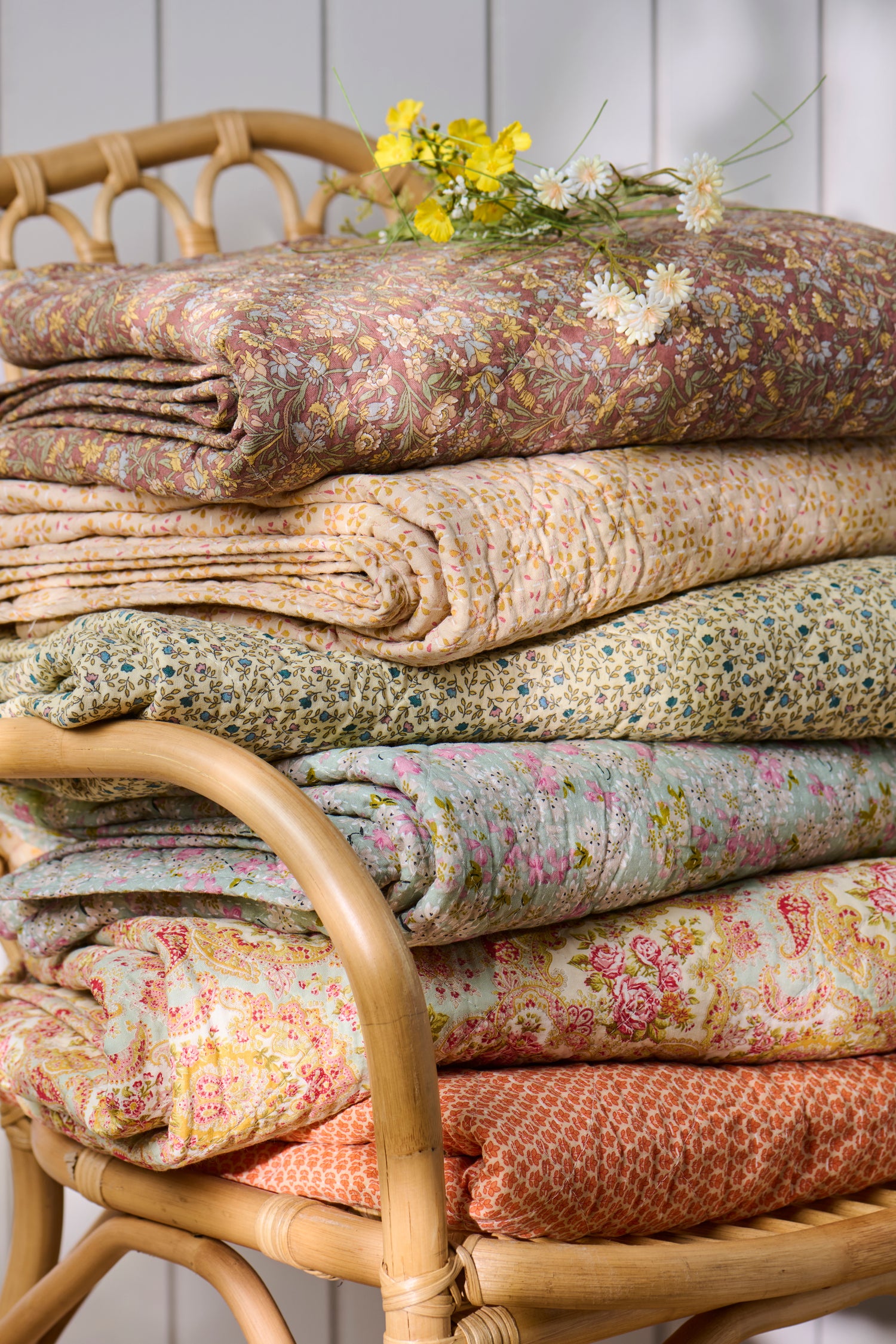 Stack of floral-patterned fabrics on a wicker chair with a white wooden panel background