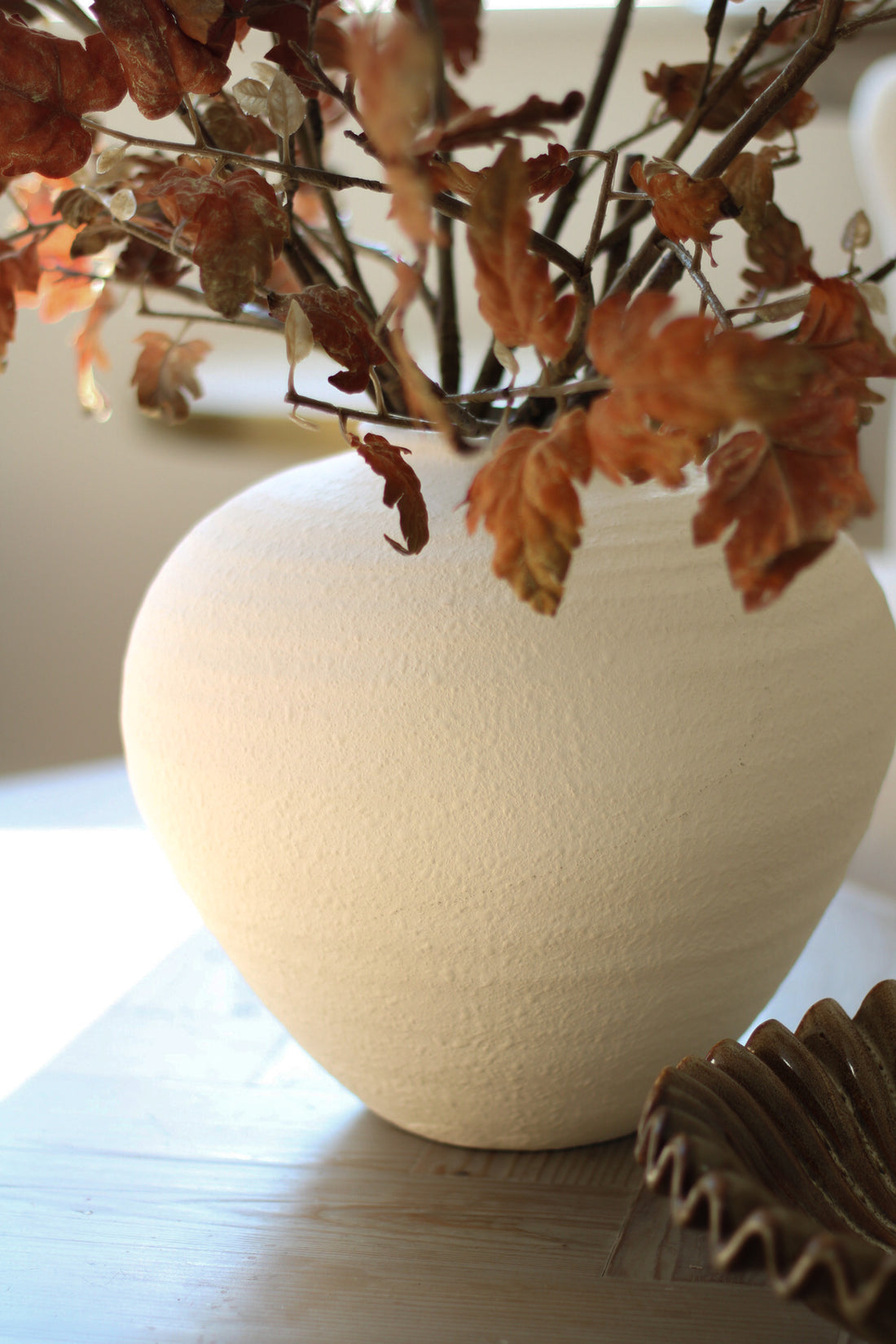 White ceramic vase with dried leaves on a wooden surface
