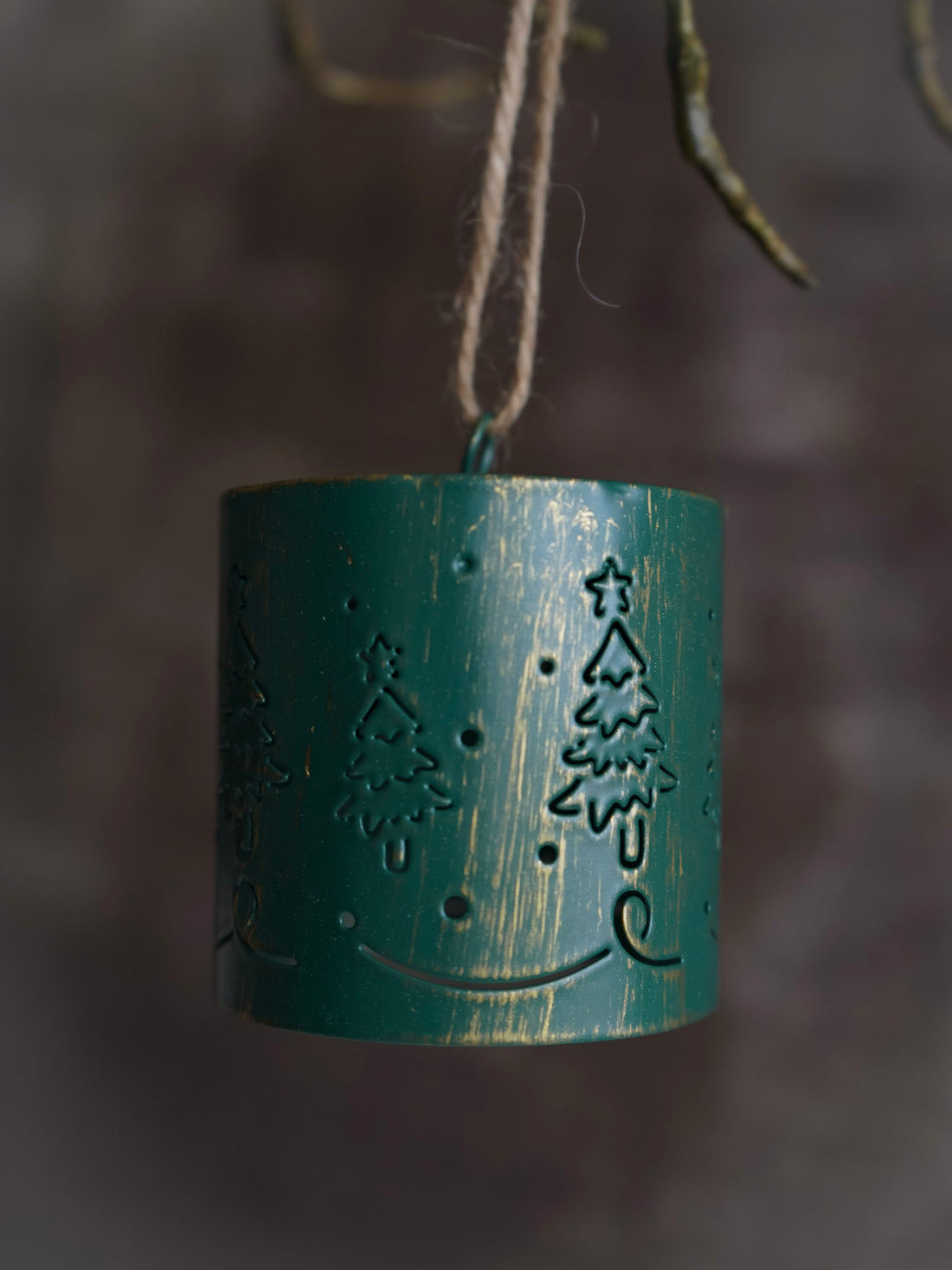 Green metal lantern with tree design hanging against a blurred natural background