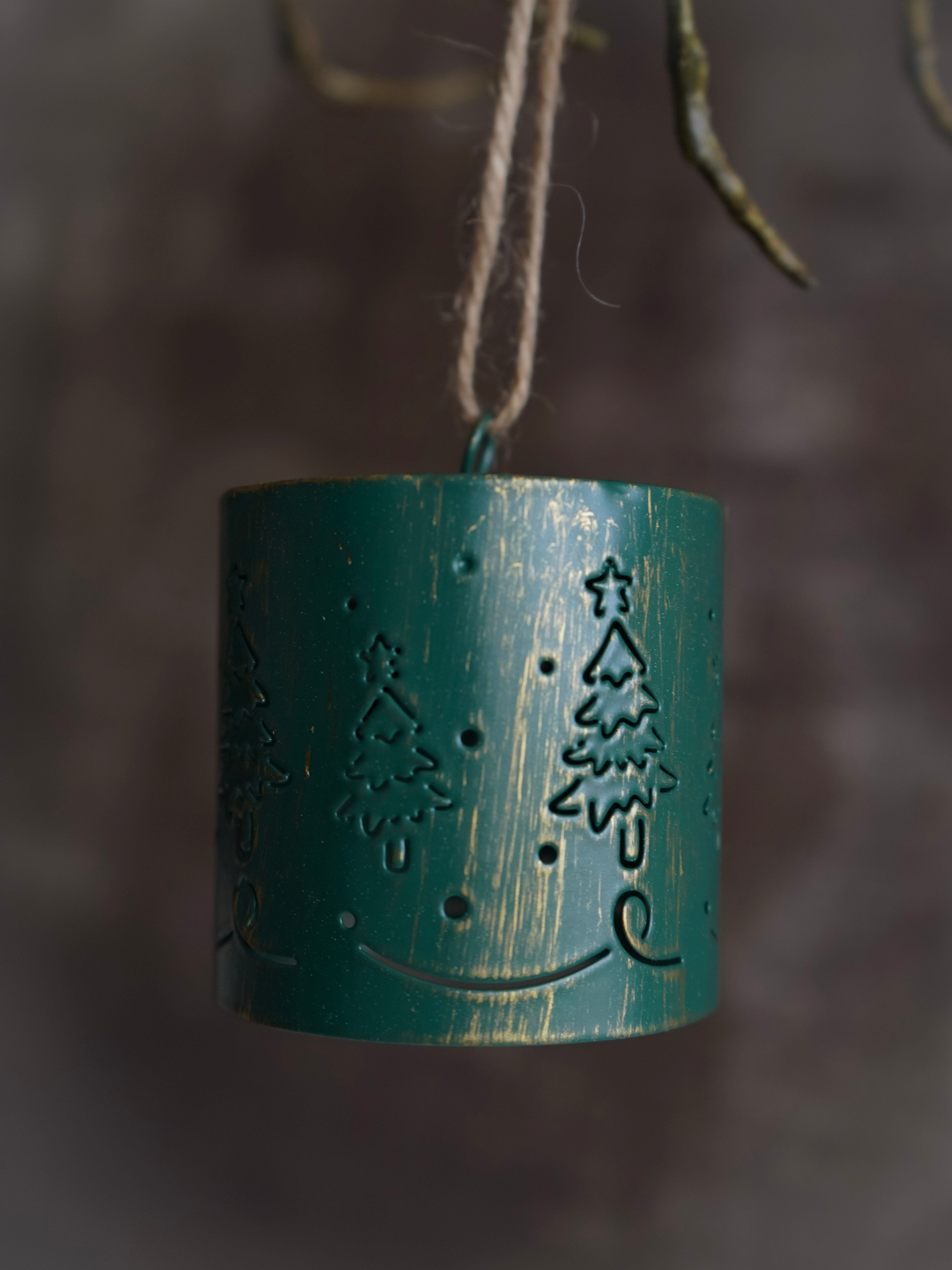 Green metal lantern with tree design hanging against a blurred natural background