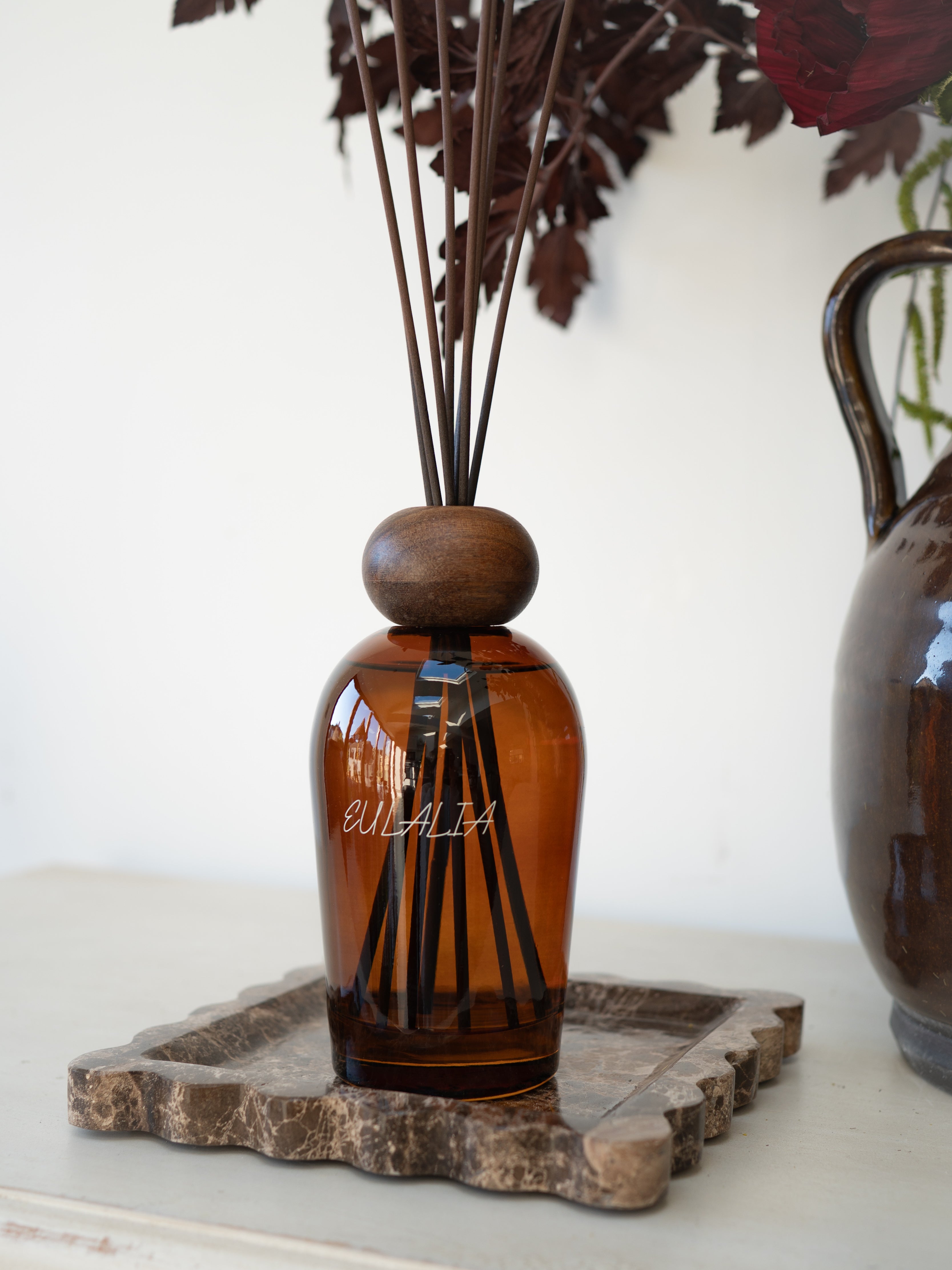Eulalia Amber Reed Diffuser on brown marble tray with brown vase in the background