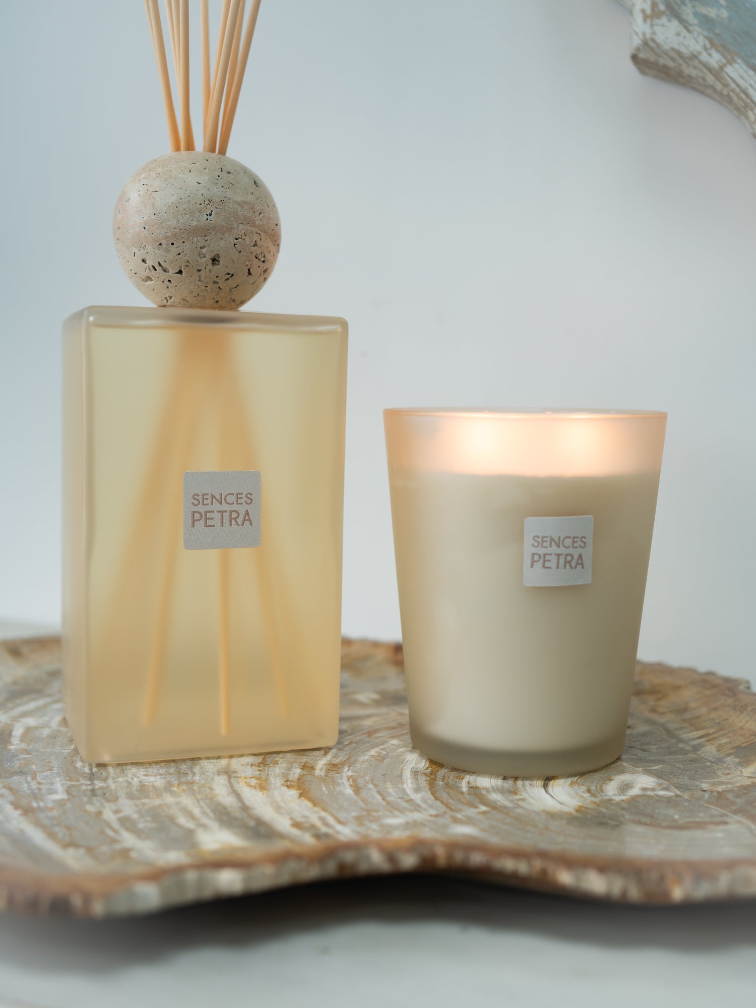 A Sences Petra reed diffuser and matching candle set on a rustic fossiled wood slice tray against a clean white background.