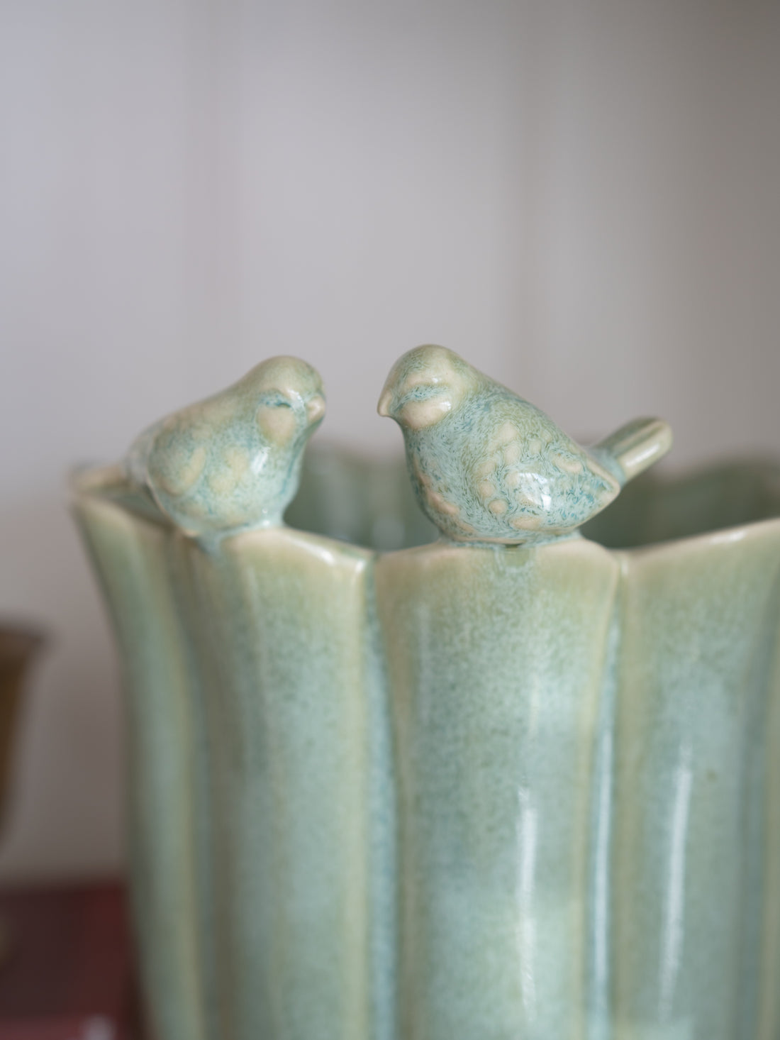Ceramic plant pot in sage green with two bird figures on a plain background