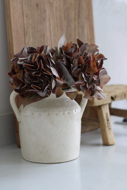 White ceramic pitcher with brown hydrangeas on a white surface