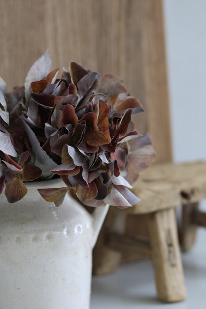 Ceramic vase with faux hydrangeas flowers on a wooden surface
