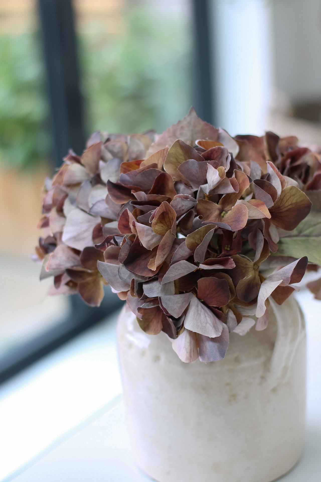 Decorative vase with pink and purple hydrangeas flowers on a windowsill