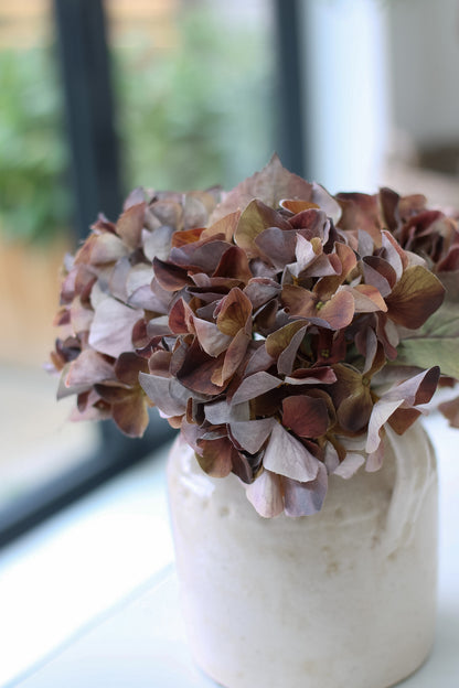 Decorative vase with pink and purple hydrangeas flowers on a windowsill