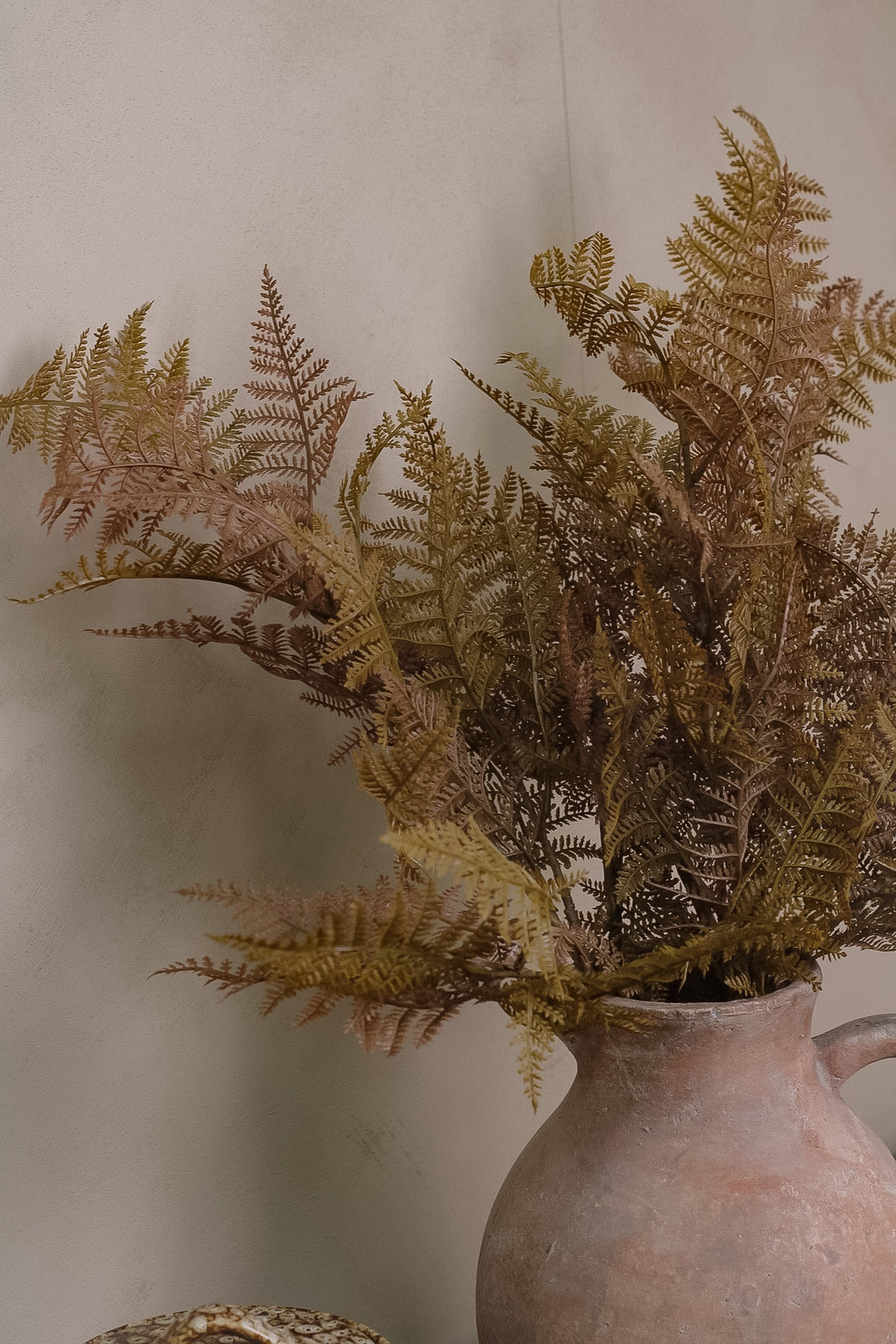 Faux ferns in a terracotta pot against a neutral background