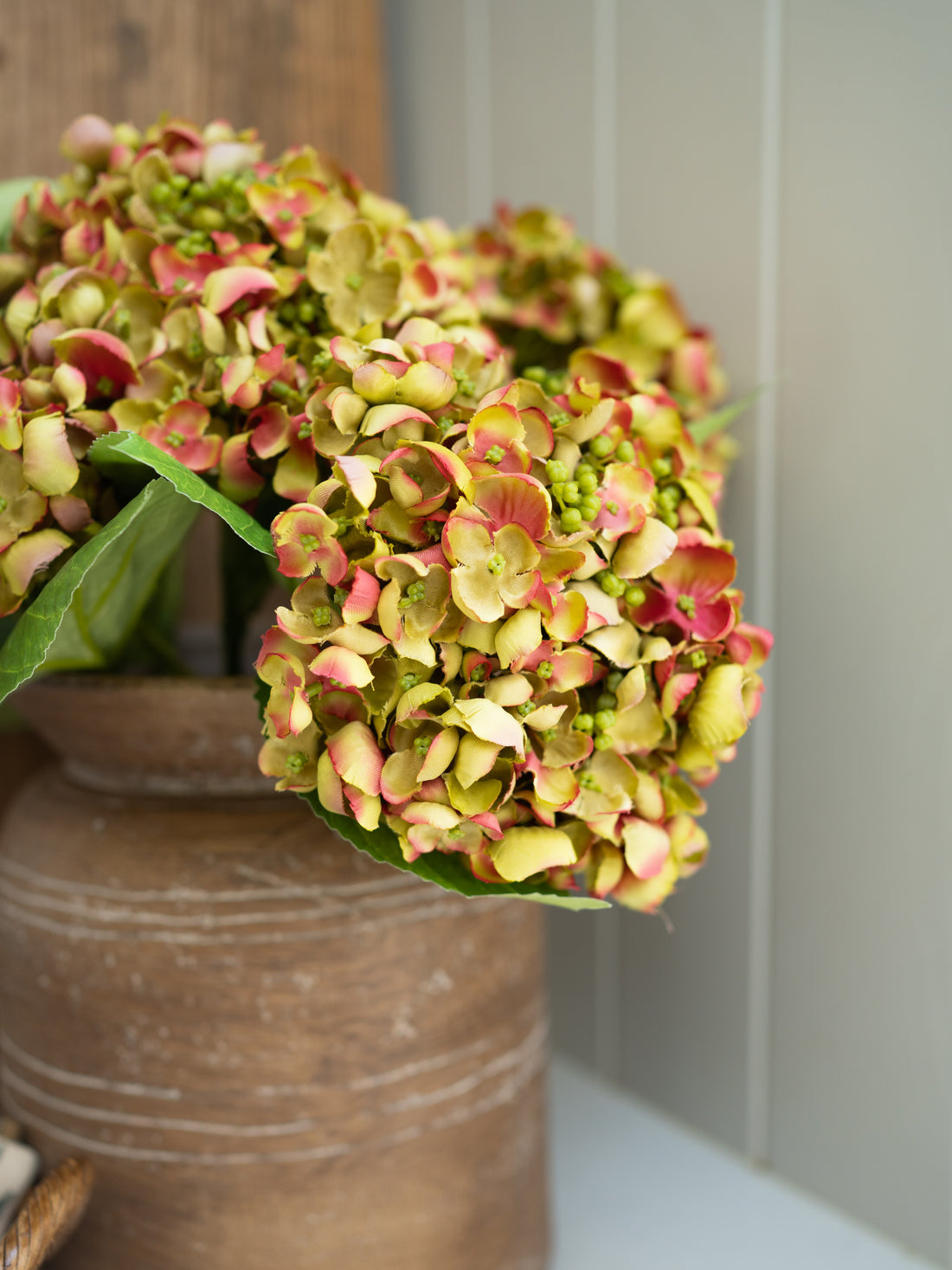 Bouquet of green and pink faux hydrangea flowers in a terracotta pot on a neutral background