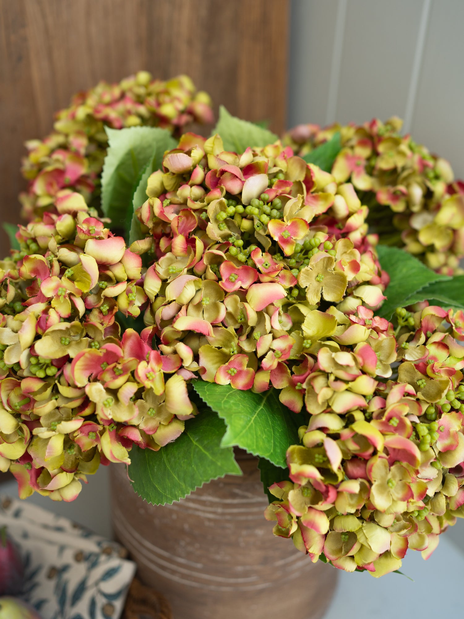 Bouquet of pink and green artificial hydrangea flowers in a vase on a wooden surface.