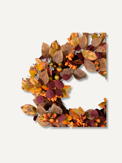An artificial autumn wreath with faux leaves in shades of brown, orange, and burgundy, accented with small orange berries and greenish-yellow fruits, shown on a light gray background.