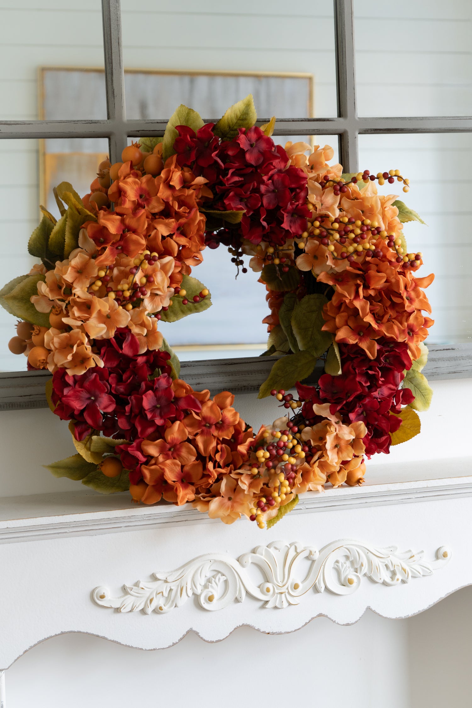 Autumn-themed faux hydrangea wreath on a white surface with a mirror in the background