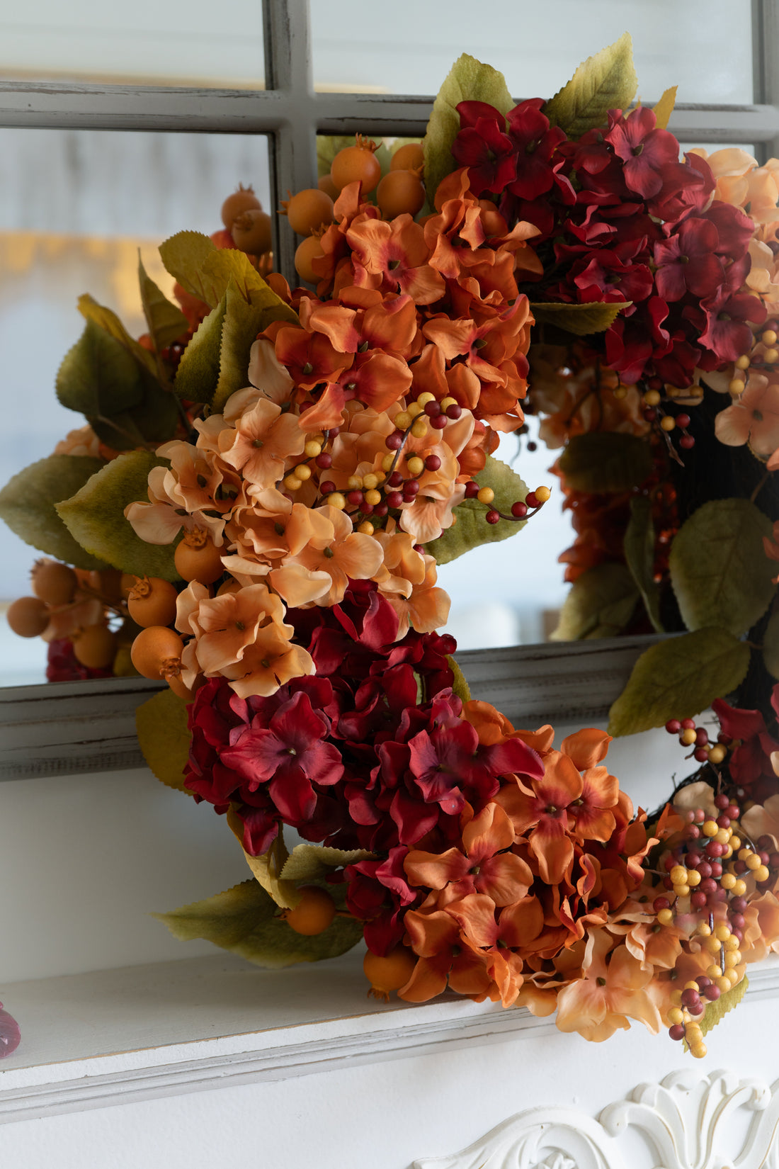 Autumn-themed faux hydrangea wreath with colorful flowers and berries on a decorative surface.