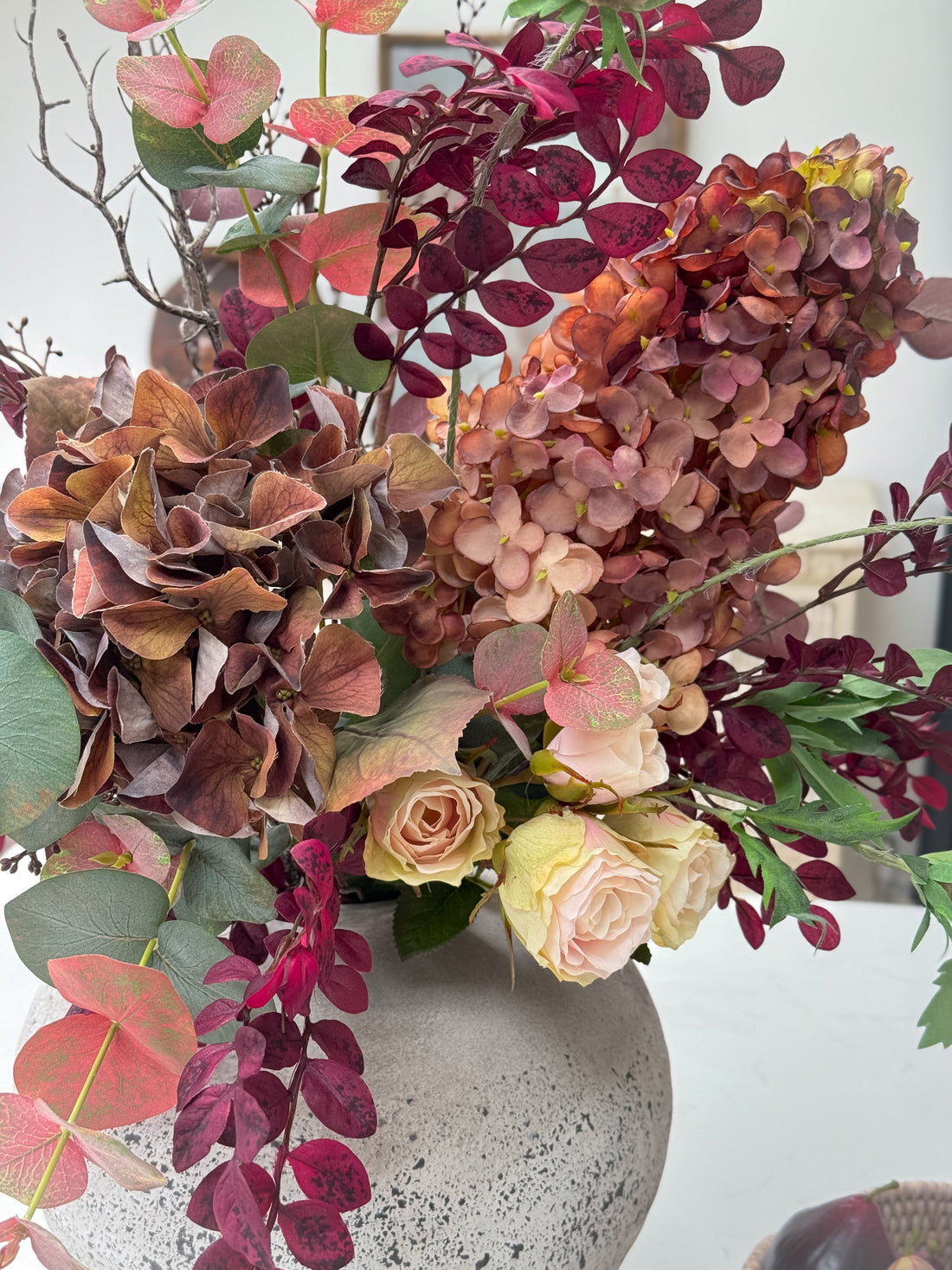 Decorative faux autumn flower arrangement with hydrangeas and roses in a textured vase.