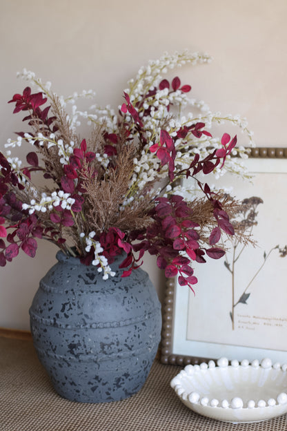 Charcoal textured vase with decorative autumn flowers on a surface with a blurred background