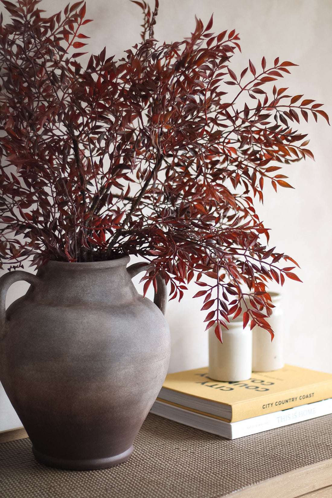 Decorative vase with red leaves on a surface with books in the background