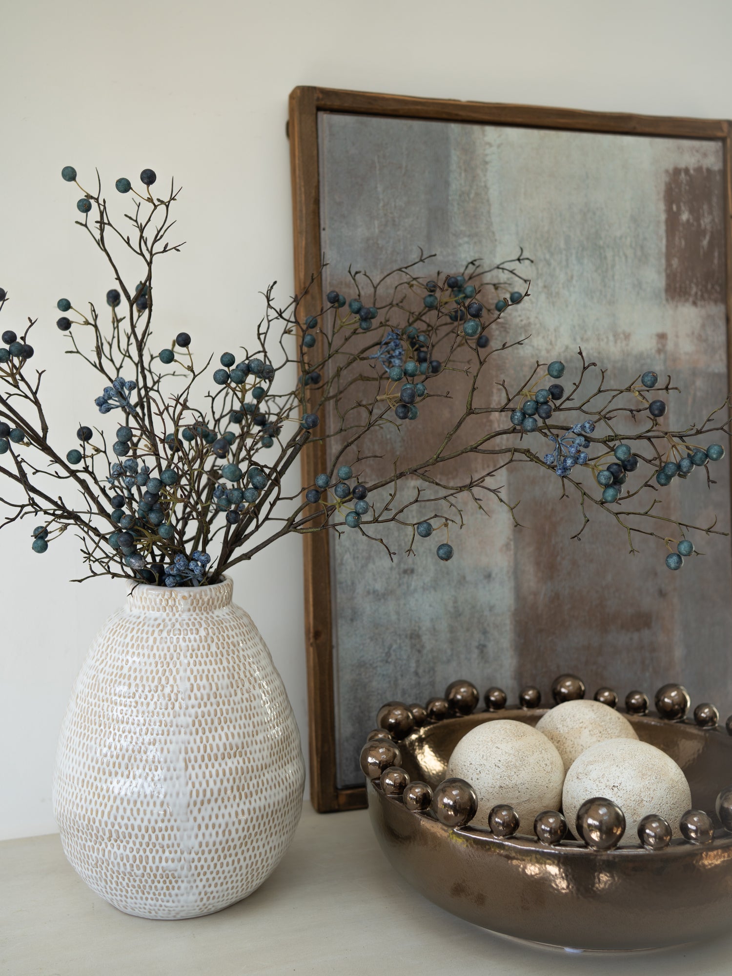 Decorative items including a textured vase with branches and berries, a gold bowl with spherical objects, and a framed abstract painting.