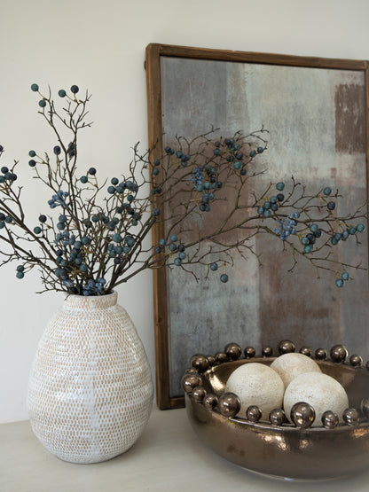 Decorative items including a textured vase with branches and berries, a gold bowl with spherical objects, and a framed abstract painting.