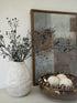 Decorative items including a textured vase with branches and berries, a gold bowl with spherical objects, and a framed abstract painting.