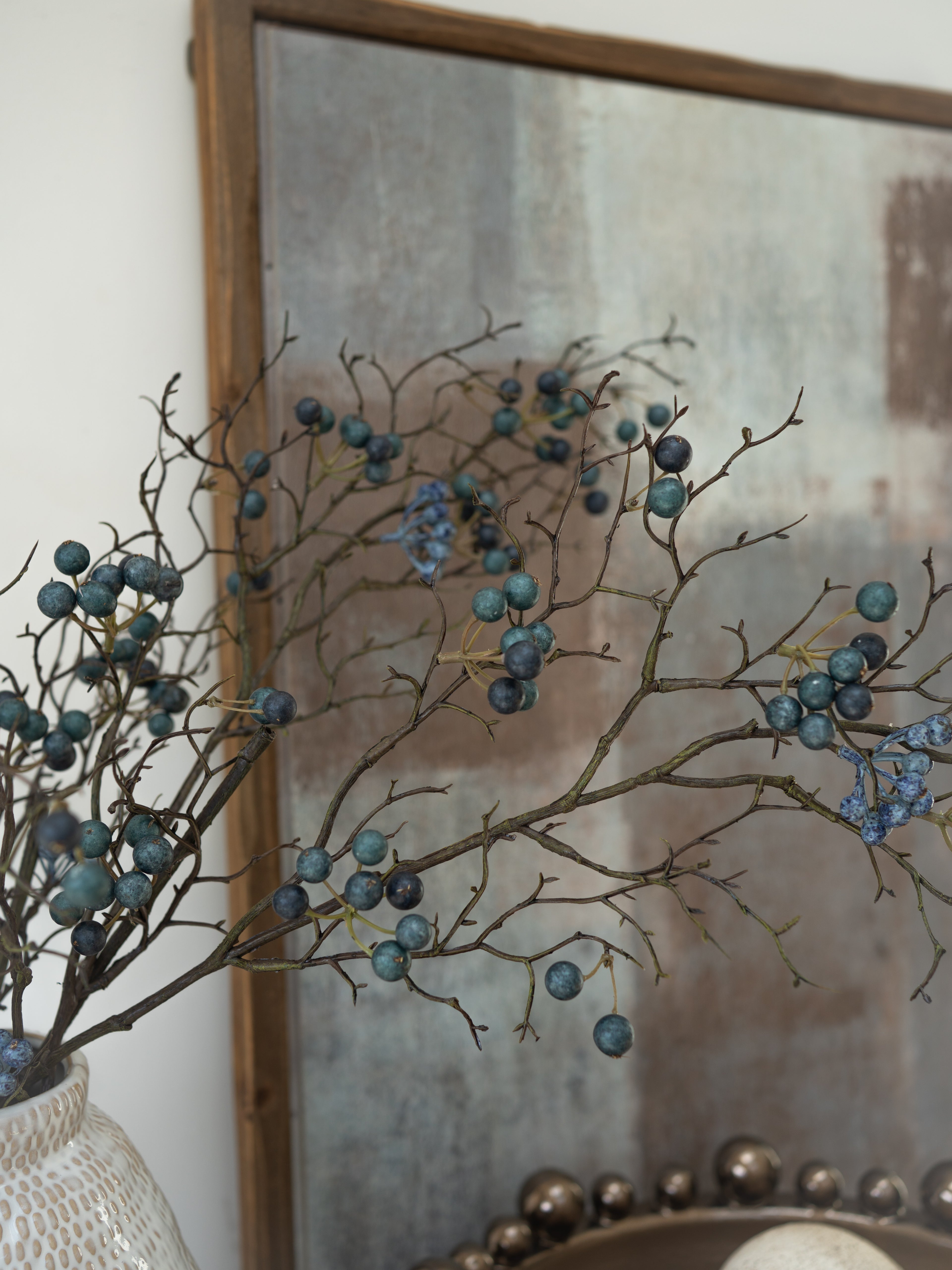 Decorative branches with faux blue berries in front of a textured mirror