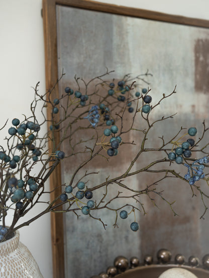 Decorative branches with faux blue berries in front of a textured mirror