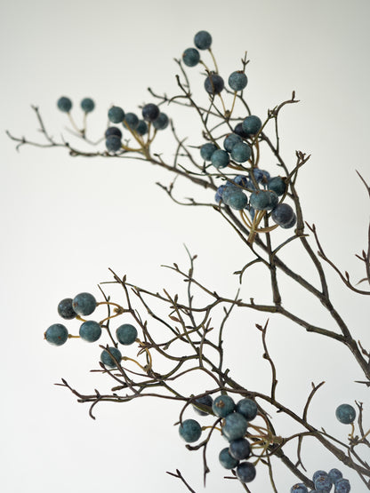 Branches with faux blue berries on a light gray background