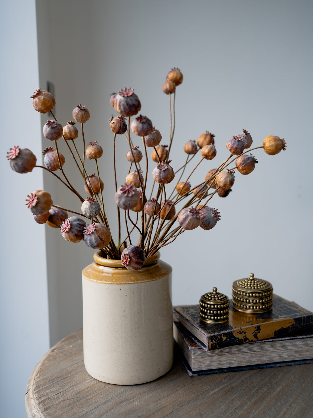 Faux Brown Poppy Head Branch in vintage salt jar with set of two brass boxes on stack of storage book boxes