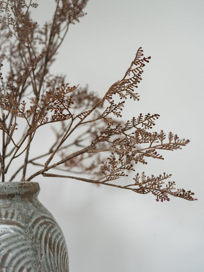Dried brown botanical branches arranged in a textured gray ceramic vase against a soft light gray background.