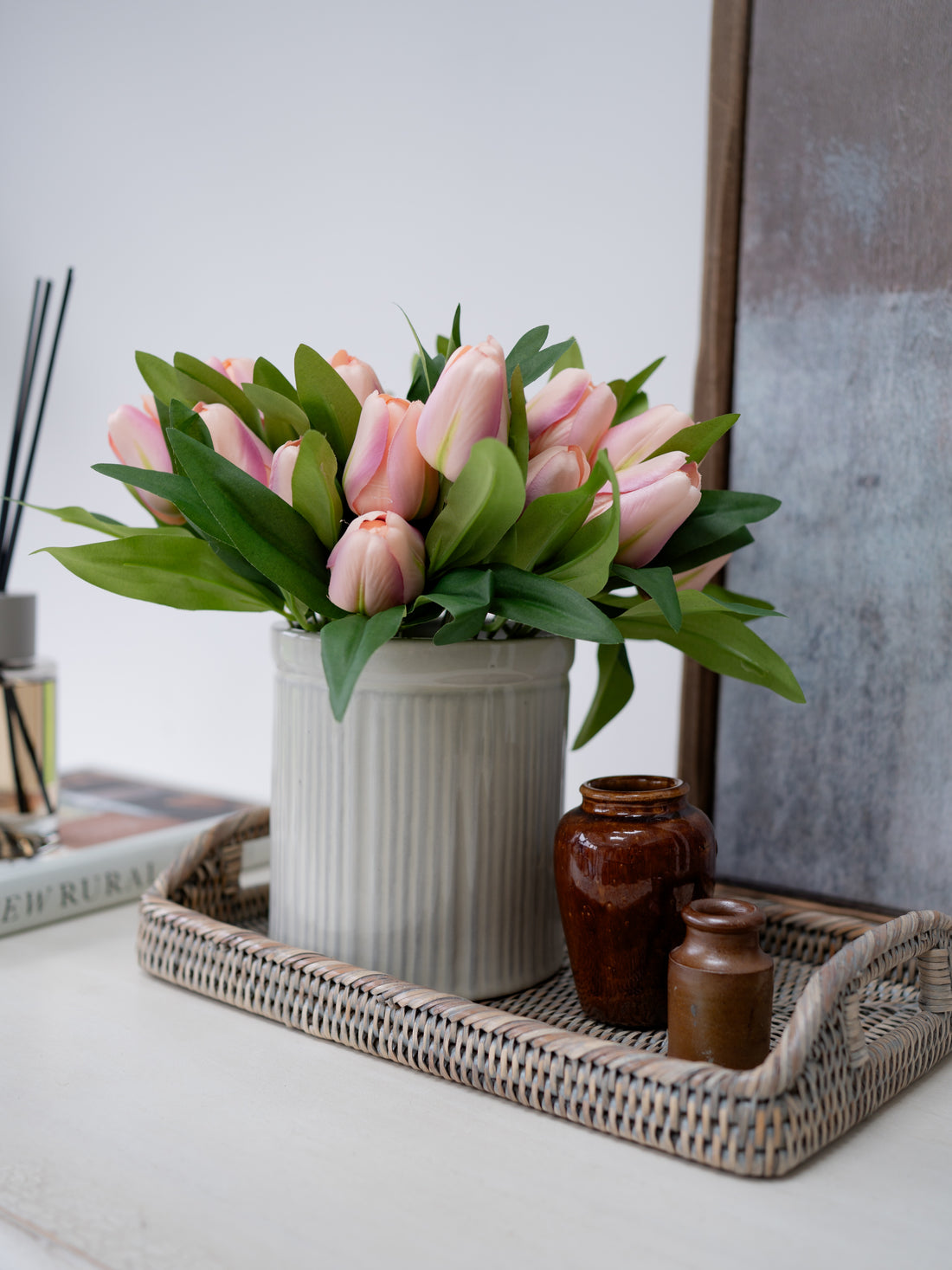 artificial Pink tulips in a white vase on a decorative tray with a neutral background