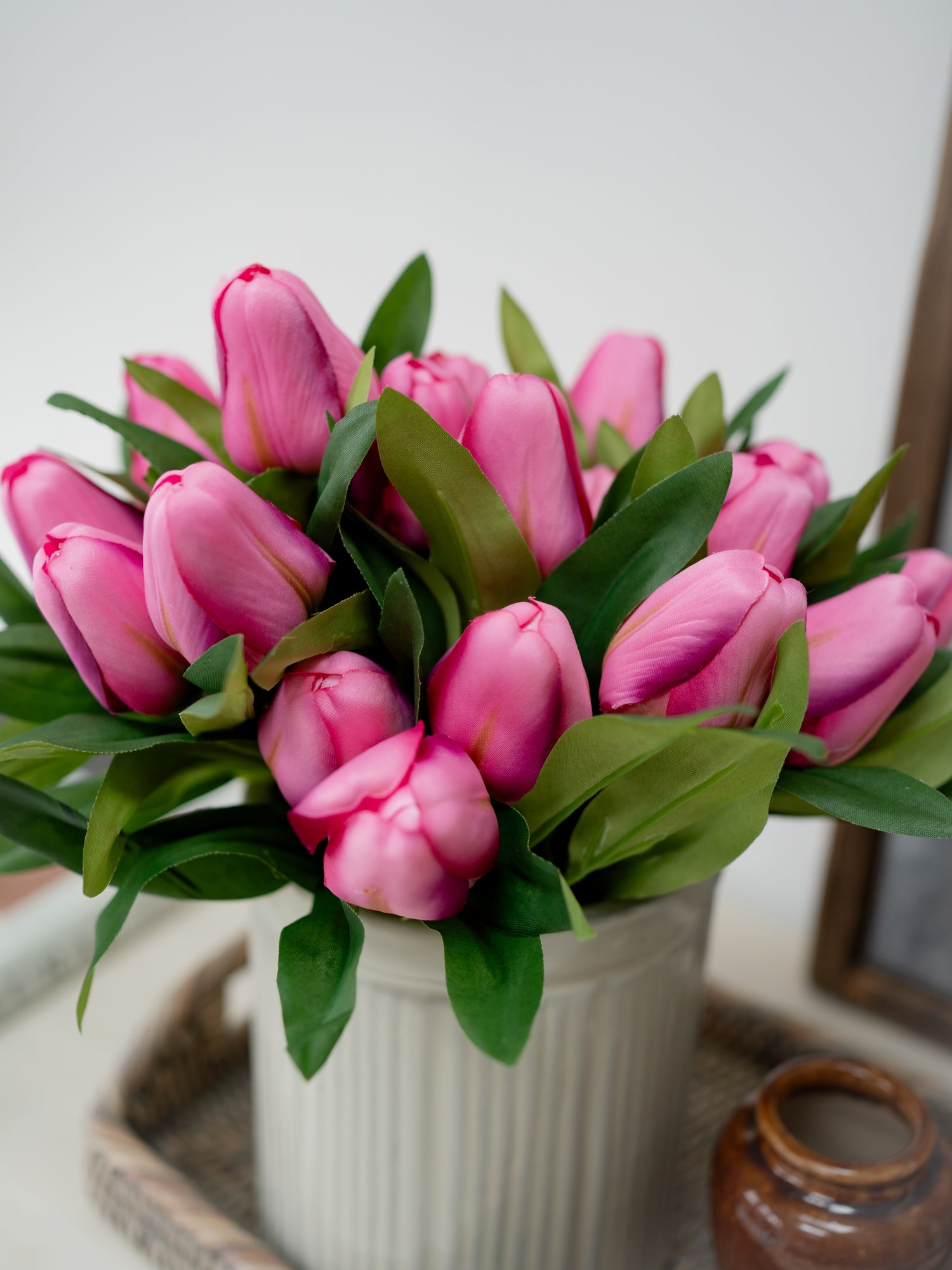 Bouquet of pink tulips in a white vase on a wooden surface with a neutral background