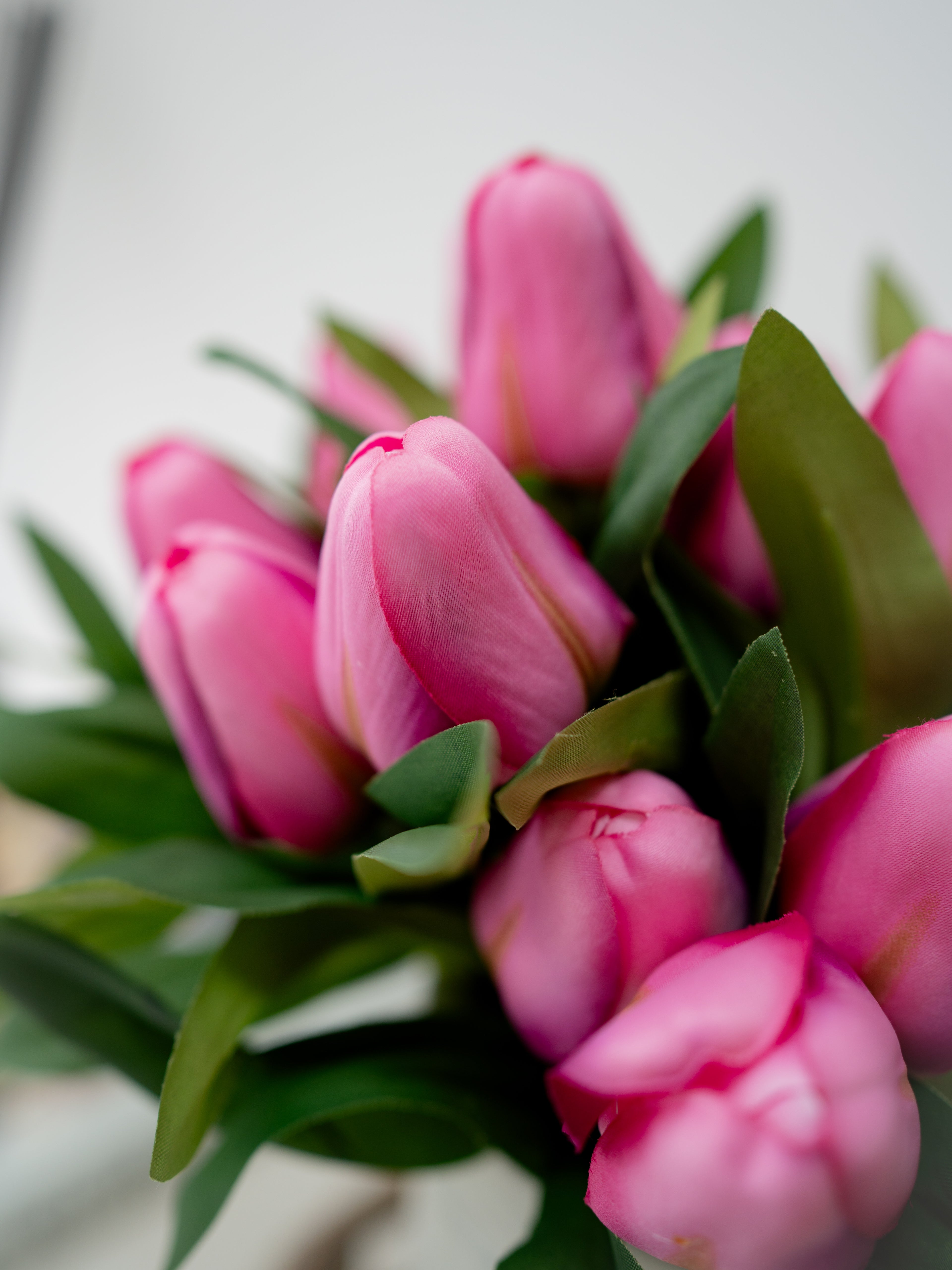 Close-up of artificial pink tulips with green leaves on a blurred background