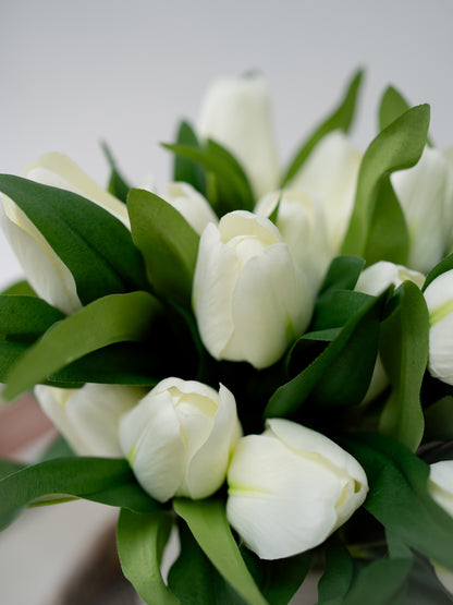 Bouquet of artificial white tulips with green leaves on a light background
