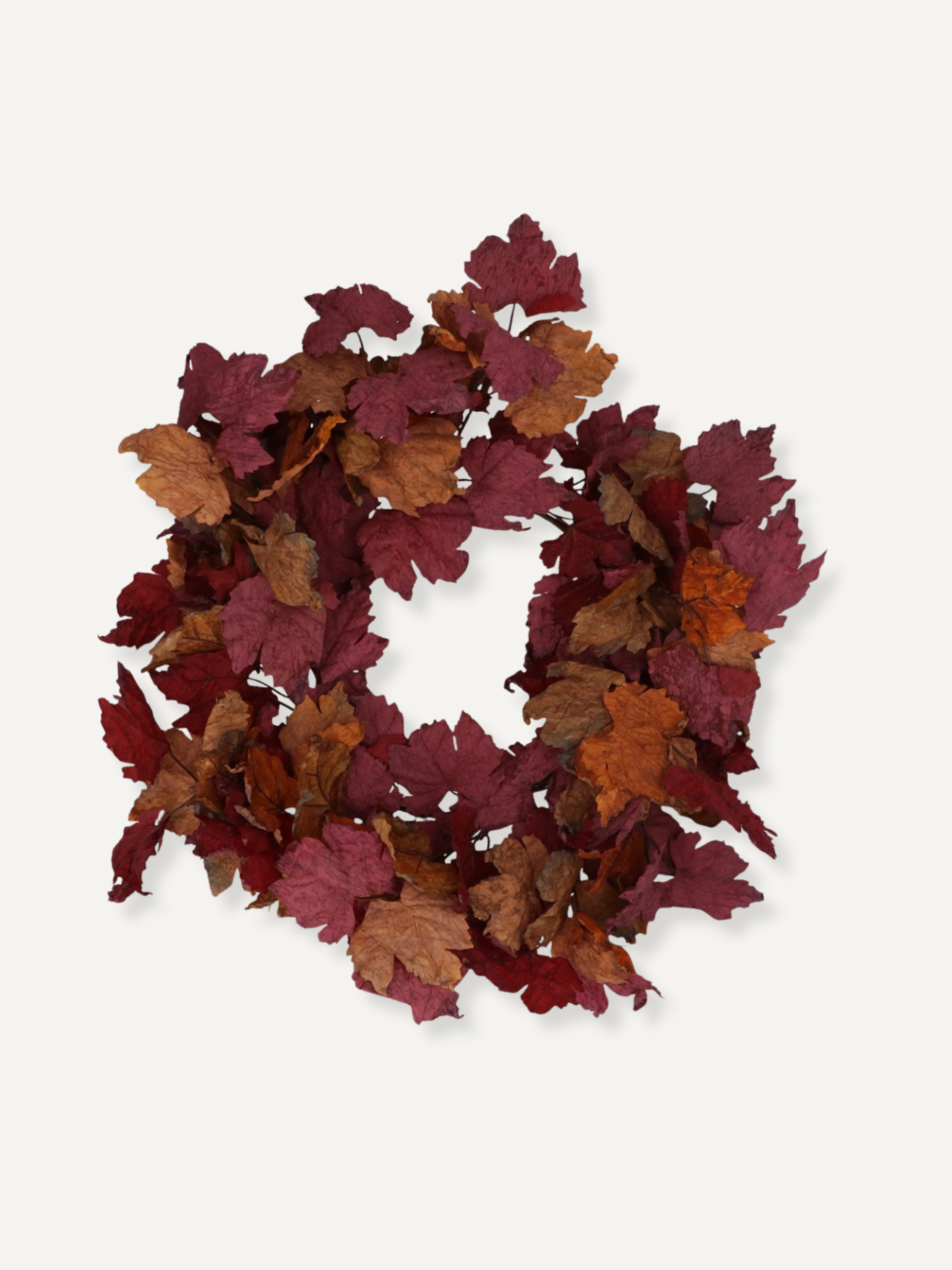 An faux autumn leaf wreath made of dried maple leaves in shades of burgundy, rust orange, and brown, photographed against a solid off-white background.