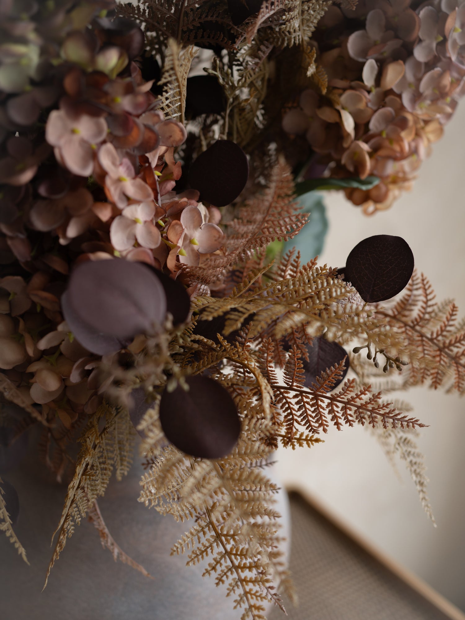 Close-up of a floral arrangement with autumn flowers and leaves on a neutral background