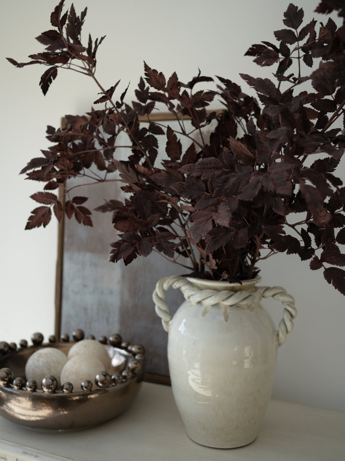 White roman inspired vase with twisted handles and with Faux Burgundy Physocarpus Diablo leaves on a white surface